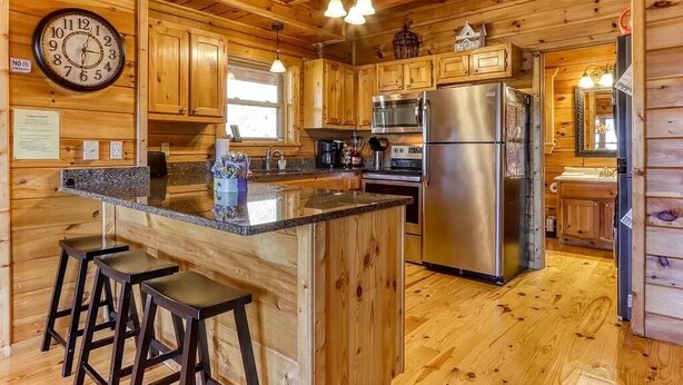 Een houten keuken in een chalet, met een centraal eiland, barkrukken, roestvrijstalen apparatuur en een klok aan de muur.