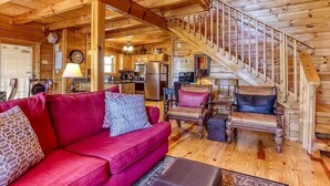 Een houten hut binnen met een rode bank, houten stoelen, een trap en een keukenhoek.