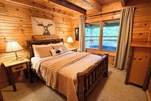 A wooden cabin bedroom with a bed, two bedside tables, a window with curtains, and a deer painting on the wall. - The Adaha Cabin rustic&cozy at Douglas Lake (Sevierville)