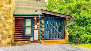 Eine Blockhütte mit Steinwand, Holztür und einem Metallzaun mit Tierkonturen.