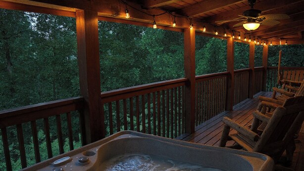 Ein Whirlpool auf einer Holzdielen Terrasse mit Blick auf Bäume, Holzstühle und Lichterketten.
