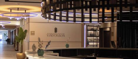 A reception area with a curved marble counter, a sign reading "Vidorada," and a modern ceiling design.