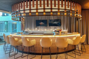 Zona de bar moderna con diseño circular, taburetes y una pantalla de televisión mostrando el nombre del hotel.