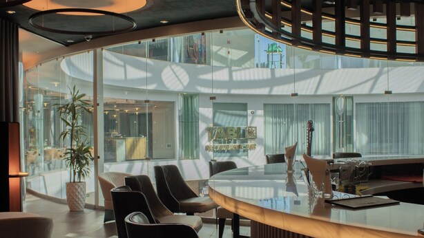 Un intérieur moderne avec un bar aux lignes courbes, un espace salon et de grandes fenêtres offrant une vue sur l’espace intérieur.