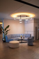 Una sala moderna con un sofá seccional gris, un otoman redondos y una mesa de centro con un jarrón de flores.