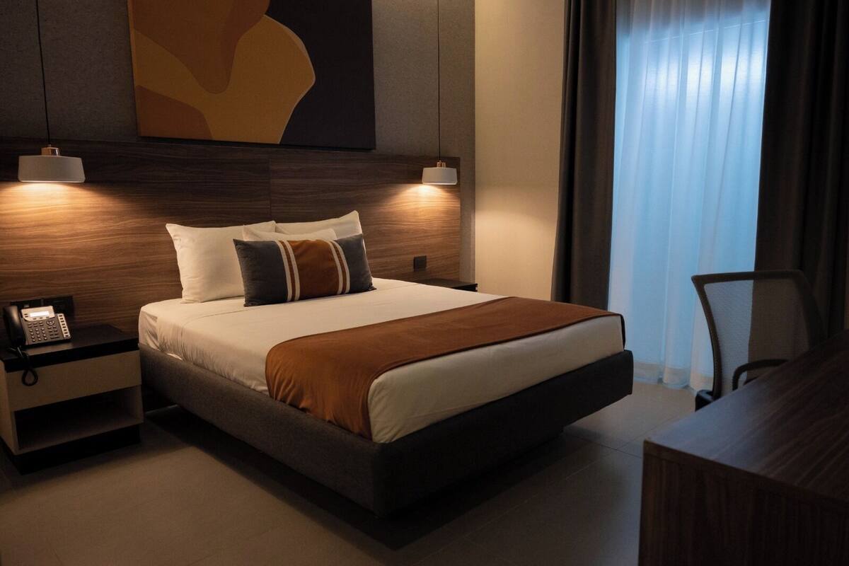 Una habitación de hotel moderna con una cama grande, lámparas de noche, un teléfono y un escritorio con una silla.
