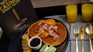 A breakfast tray with pancakes, bacon, gold coins, jam, butter packets, and a menu for a hotel casino restaurant.