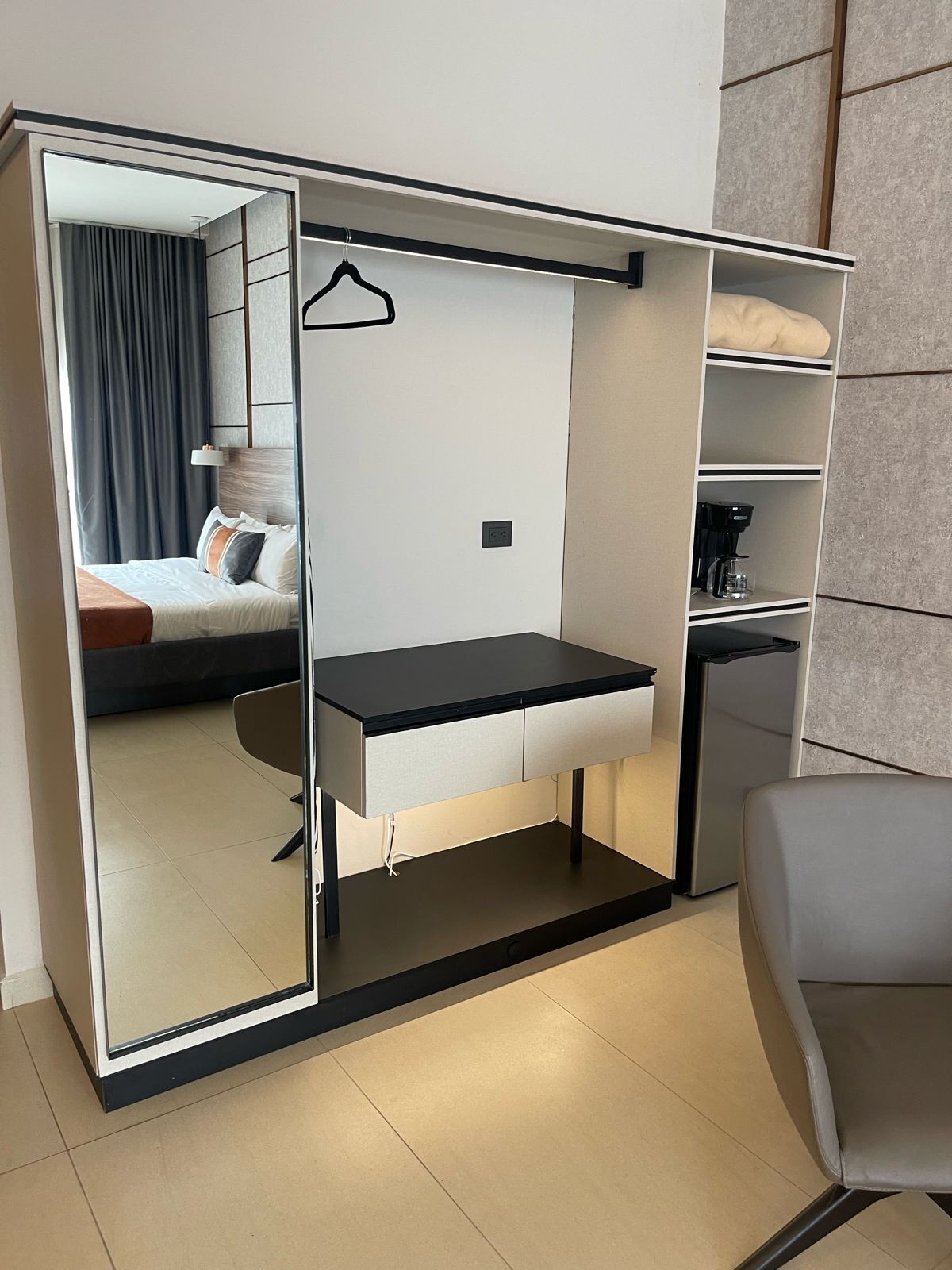 Una habitación moderna con escritorio integrado, perchero, cama con vistas y cafetera.