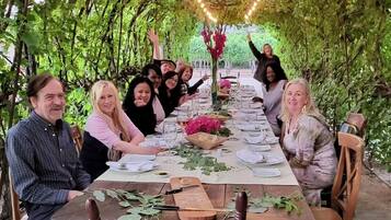 Um grupo de pessoas sentadas ao redor de uma mesa comprida com bancos de madeira, rodeadas por vegetação e luzes de corda.