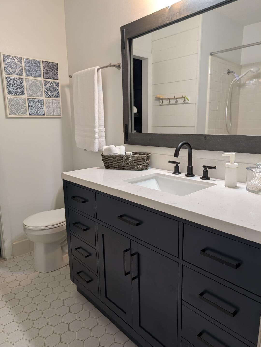 Casa de banho moderna com lavatório branco, toucador preto e espelho grande. Apresenta azulejos decorativos na parede e sanita branca.