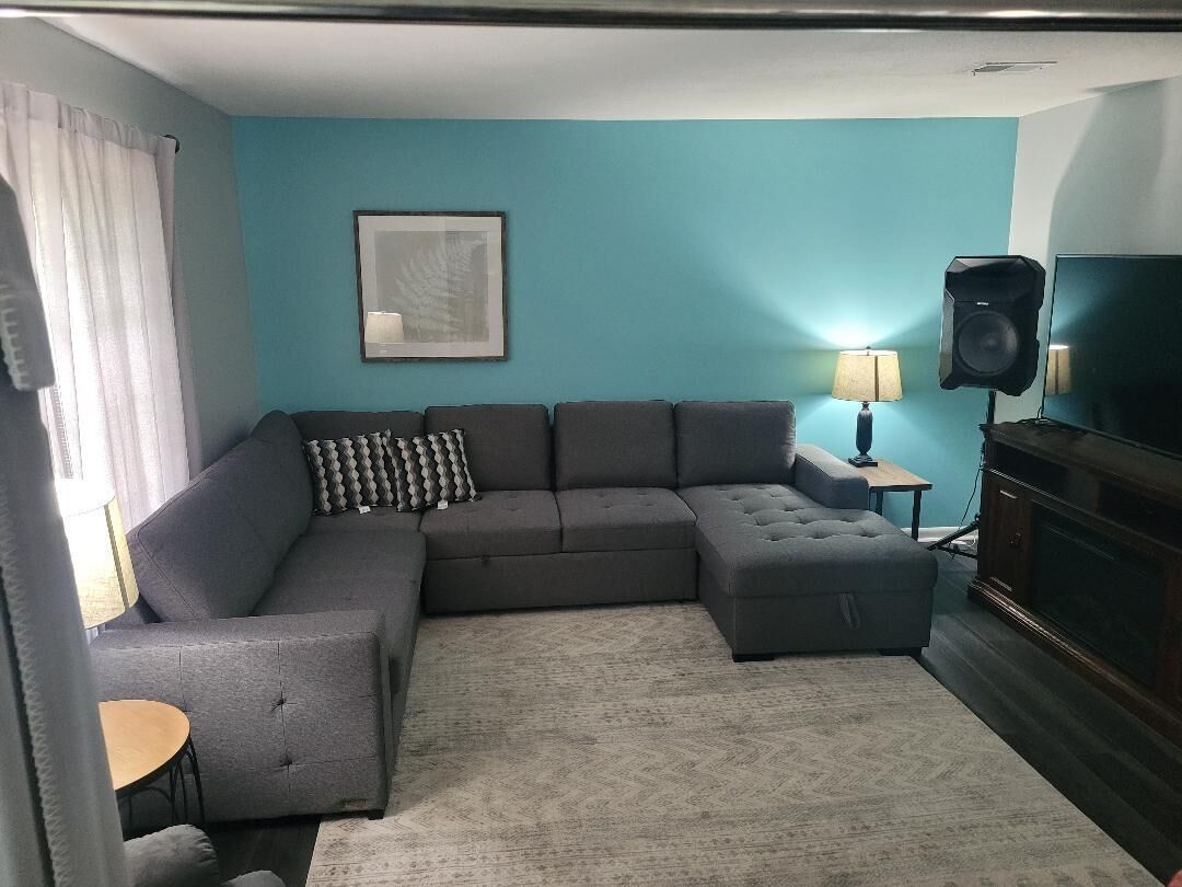 Una sala de estar con un sofá modular, una mesita redonda, un televisor y un altavoz.