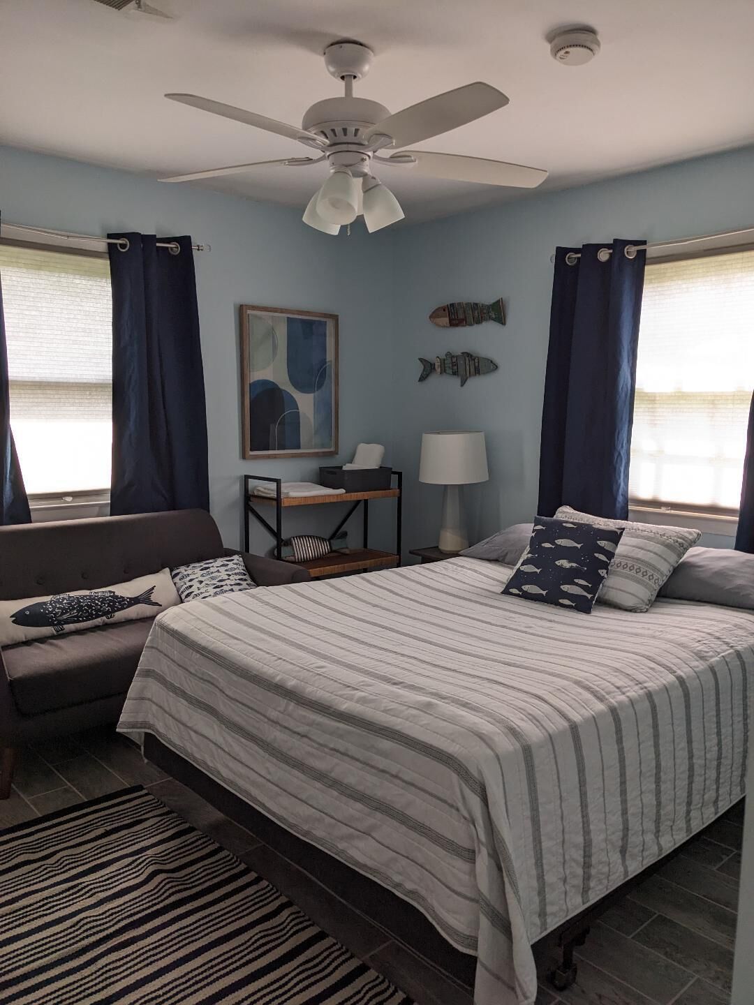 Een slaapkamer met een bed, een stoel, een bureau, een lamp en een plafondventilator.