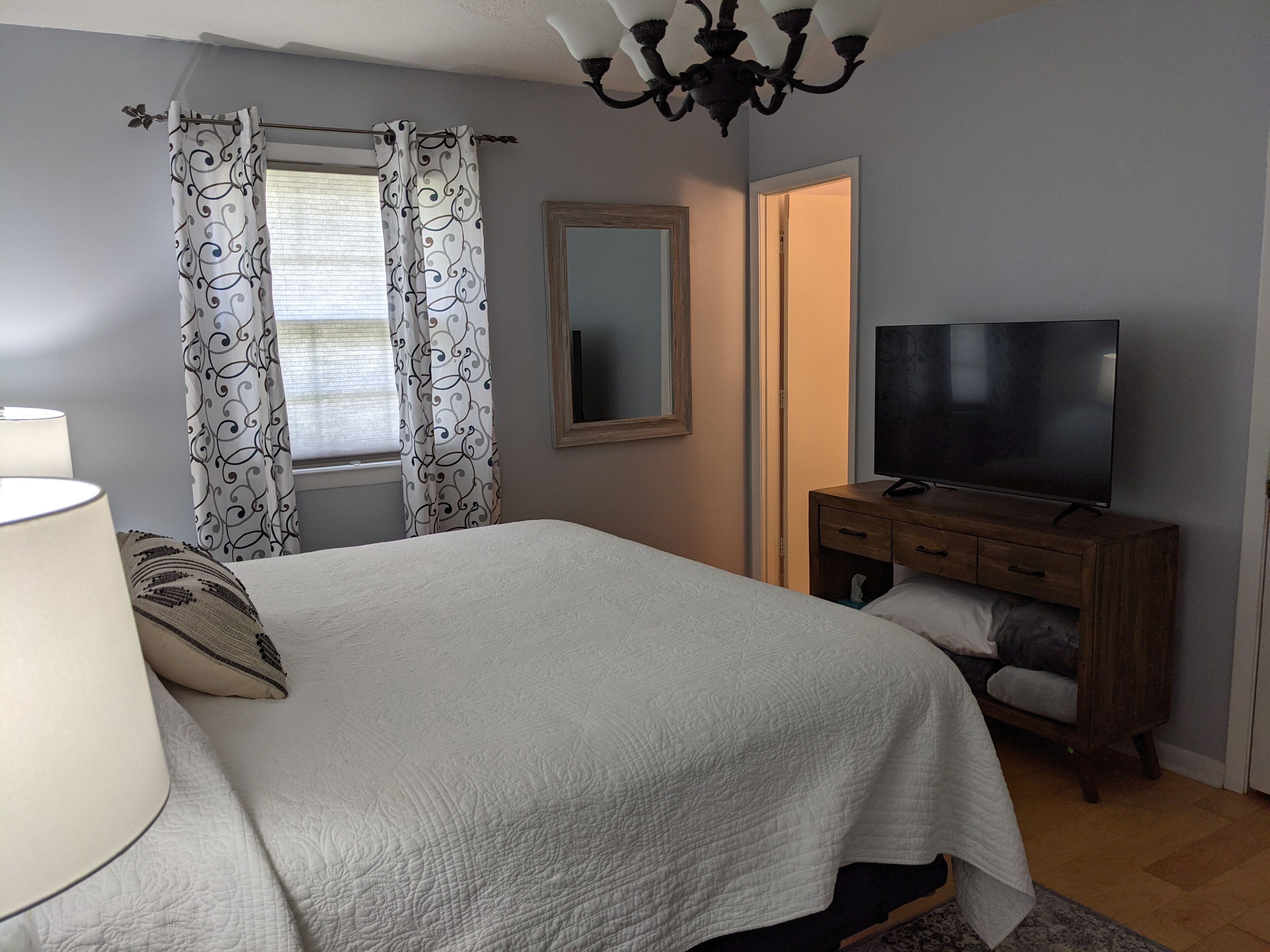 A bedroom with a bed, a TV, a dresser, a mirror, and curtains.