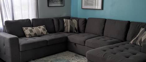 A living room with a sectional sofa, a patterned rug, and two framed pictures on the wall.