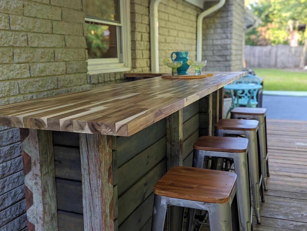 A wooden bar with stools, a blue pitcher, and glasses on a deck.