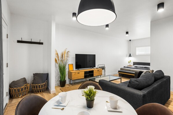 Un salon moderne avec un téléviseur à écran plat, un canapé gris et une table à manger avec des chaises.