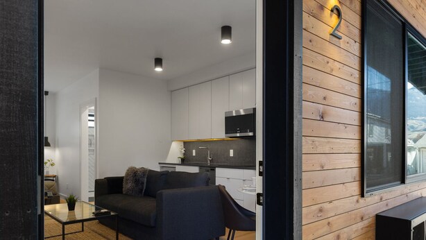 Un interior moderno con una pared de madera, un sofá, una mesa de centro de vidrio y una zona de cocina.