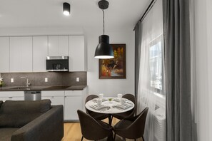Une cuisine moderne avec des armoires blanches, une hotte en acier inoxydable et un coin repas doté d’une table ronde prévue pour quatre personnes.