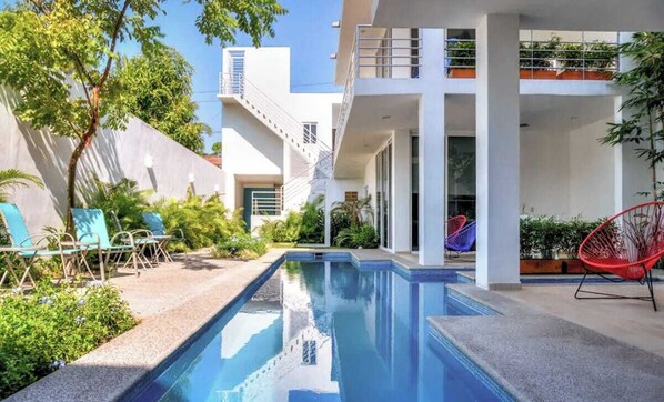 A modern pool area with a clear pool, a red chair, and a staircase leading to an upper level.