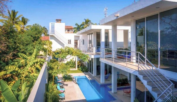 A modern building with a pool, surrounded by lush greenery.