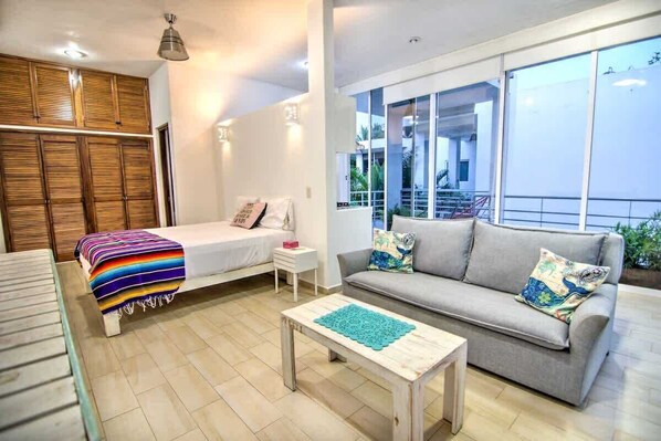 A modern living room with a bed, sofa, and coffee table, large windows, and a balcony.