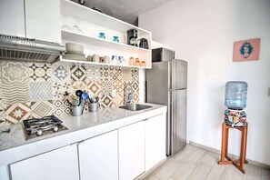 A modern kitchen with a stainless steel refrigerator, white cabinets, patterned backsplash, and a water dispenser on a wooden stand.