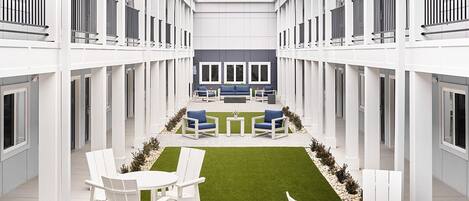 A modern courtyard with white furniture, a central seating area, and a small lawn.