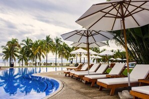 A poolside area with lounge chairs and umbrellas, surrounded by palm trees.