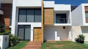 A modern multi-story residential building with a flat roof, large windows, and a well-maintained lawn.