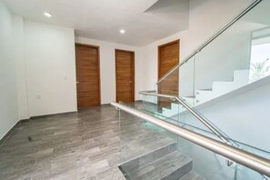 A modern interior with a glass staircase, grey tiled flooring, and wooden doors.
