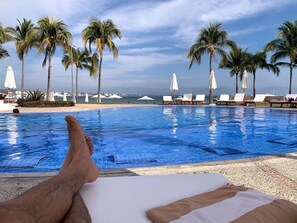 A poolside view with a clear blue pool, lounge chairs, and palm trees.