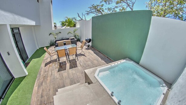A modern outdoor patio with a hot tub, a dining area with chairs, and a small pool.