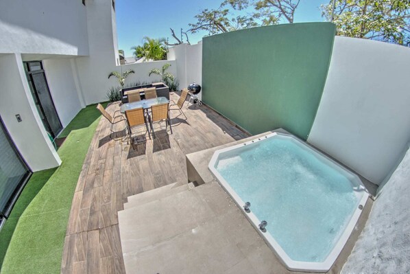 Un patio moderno al aire libre con un jacuzzi, un área de comedor con sillas y una pequeña piscina.