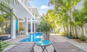 Un espace piscine moderne avec des chaises longues, une piscine et des plantes tropicales.