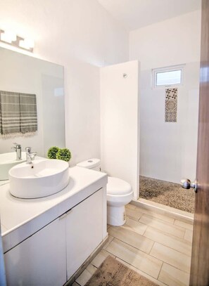 Un baño moderno con un espejo grande, un lavamanos redondo, un inodoro y una zona de ducha.