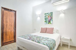 Une chambre avec une porte en bois, un lit avec une literie à motifs, une œuvre d’art accrochée au mur et une table de chevet.