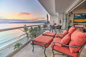 A balcony with a view of the sea and mountains, furnished with red cushioned chairs and a table. - Beachfront 2BR w Office & Panoramic Views: Nova105 (Bucerías)
