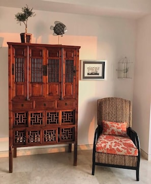 A traditional wooden cabinet with intricate carvings, a chair with a patterned cushion, and a framed picture on the wall.