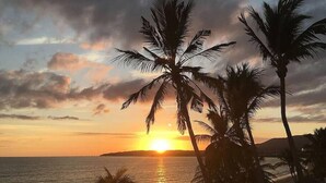 Un atardecer sobre una playa con palmeras y un mar tranquilo.