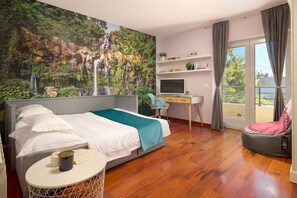 Une chambre avec un lit, un bureau, une chaise, une télévision et un balcon avec vue.