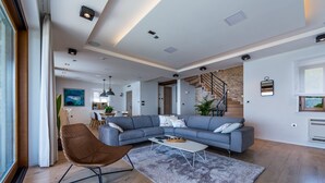 Un salon moderne avec un canapé d’angle gris, un fauteuil en osier marron et une table basse blanche.