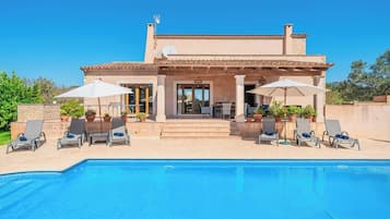 Una villa moderna con piscina, mobiliario exterior y fachada de piedra.
