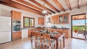 Une cuisine spacieuse avec des meubles en bois, un coin repas avec une table pour quatre personnes et une vue sur l’extérieur grâce à une porte vitrée.