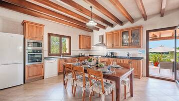 Una cocina amplia con armarios de madera, un comedor con mesa dispuesta para cuatro personas y vistas al exterior a través de un ventanal.