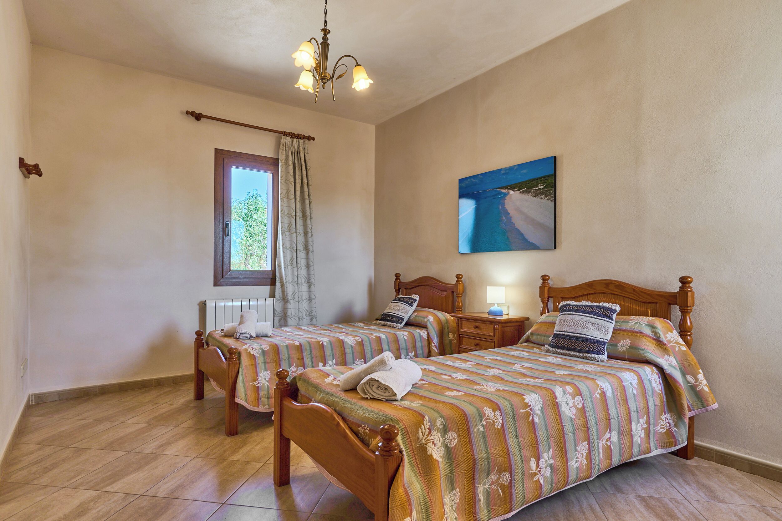 Quarto com duas camas de madeira, uma janela com cortinas, um quadro na parede e um candelabro.