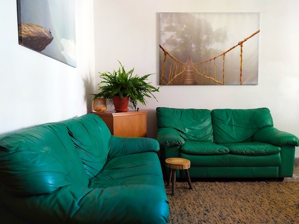 A living room with two green sofas, a small wooden stool, a potted plant, and a painting of a bridge. - Maison Manaar... a cozy retreat just a stone's throw from the sea! (Polignano a Mare)