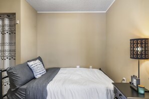 Une chambre à coucher avec un lit, des oreillers, une table de chevet avec une lampe et une prise électrique fixée au mur.