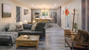 Een moderne woonkamer met een bank, salontafel en een eethoek, met een keuken op de achtergrond.