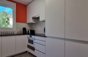 A modern kitchen with white cabinets, a black countertop, and a red accent wall.