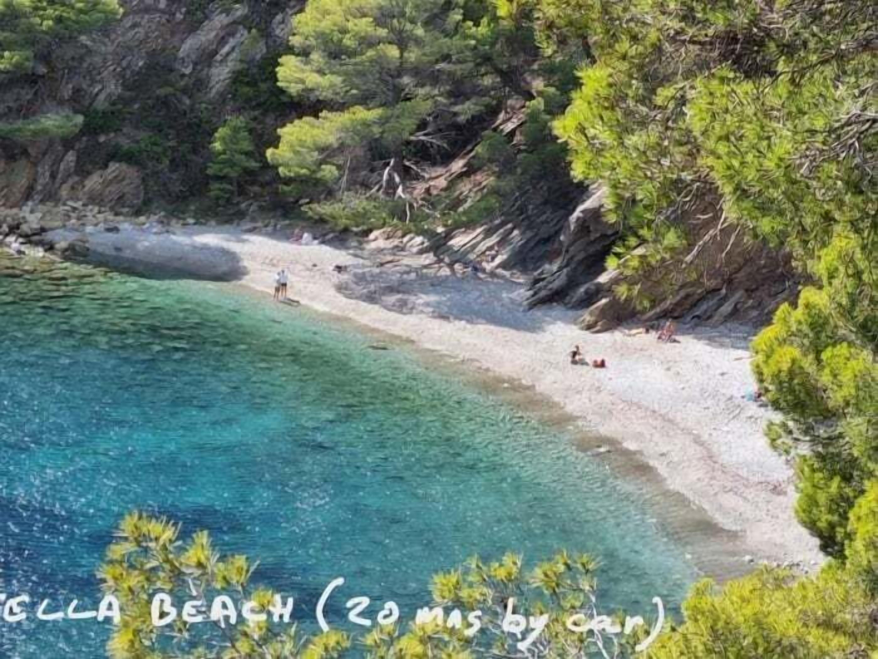 Ein Strand mit klarem türkisblauem Wasser, steinigen Klippen und dichtem Grün.